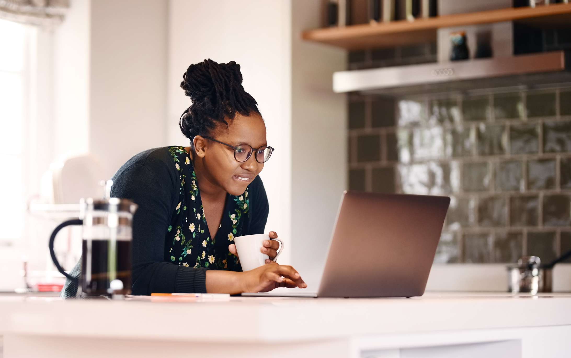 A woman uses a laptop and drinks coffee.