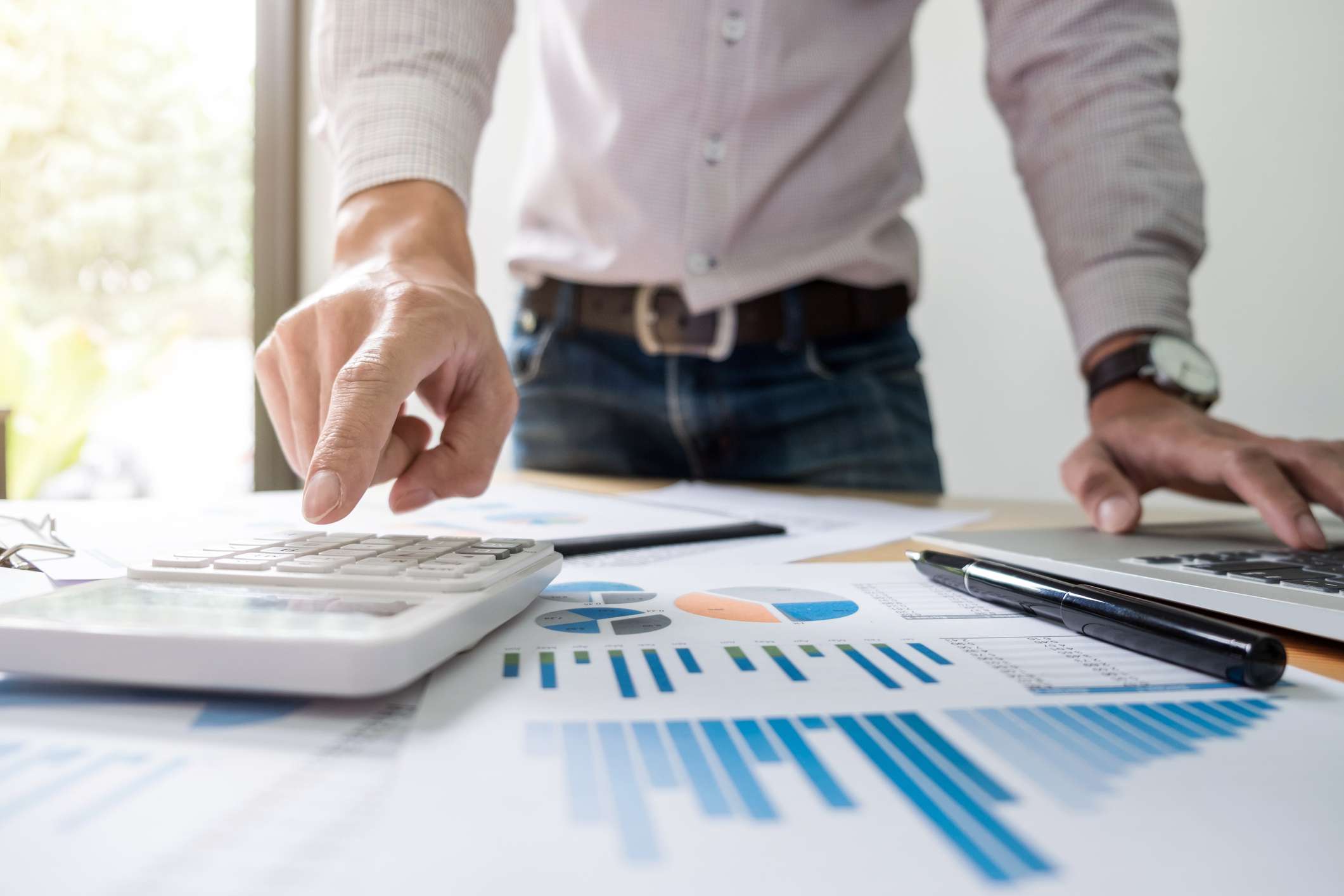 A businessman analyzing graphs and documents, using a calculator.