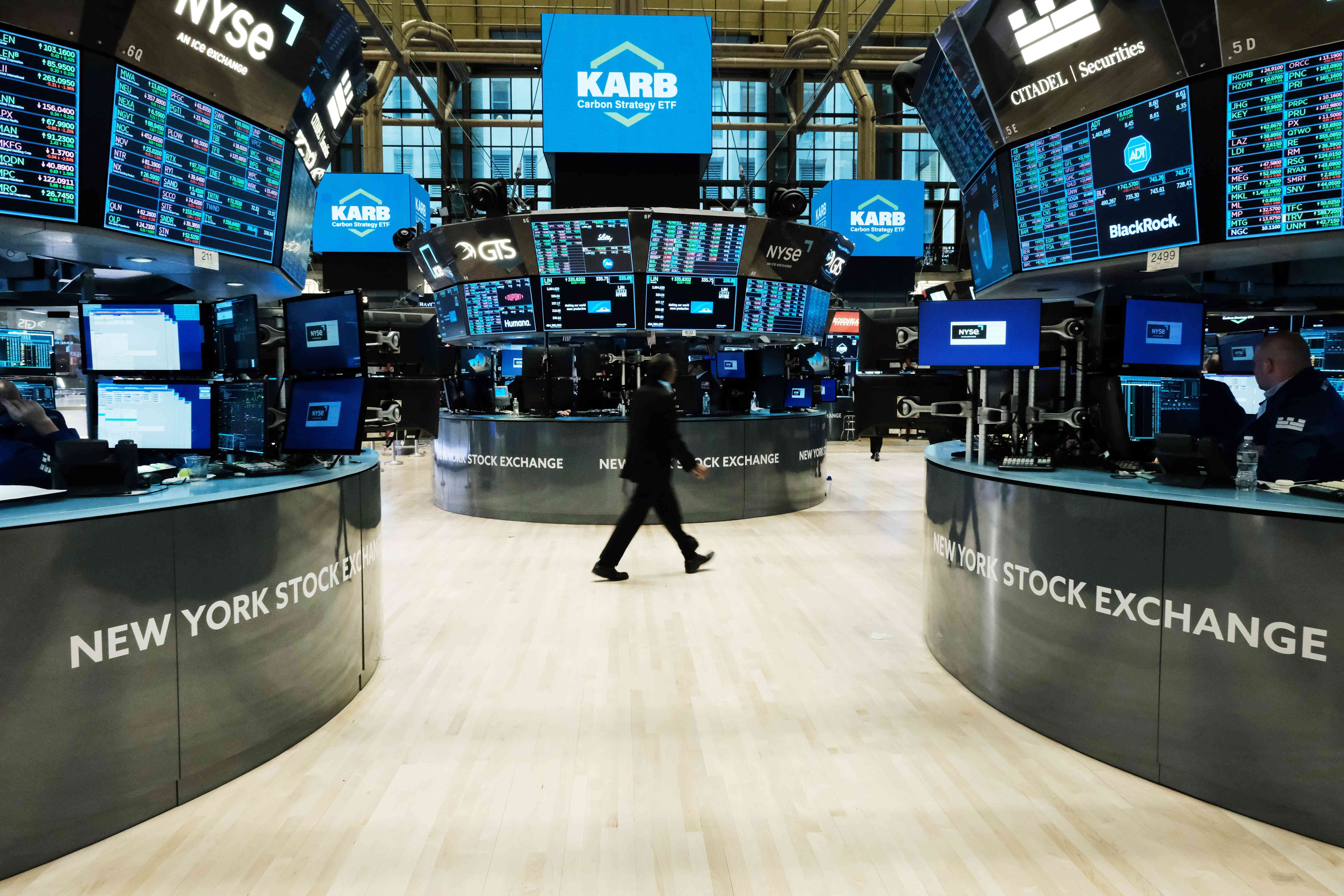 A trader walks past desks and TV screens on the floor of the New York Stock Exchange